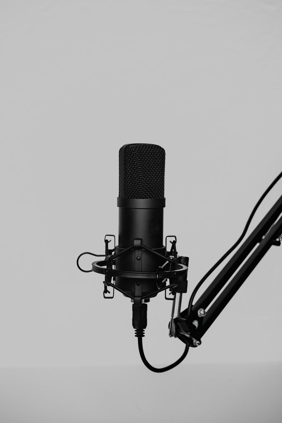 A black studio microphone on a boom arm against a grey background.