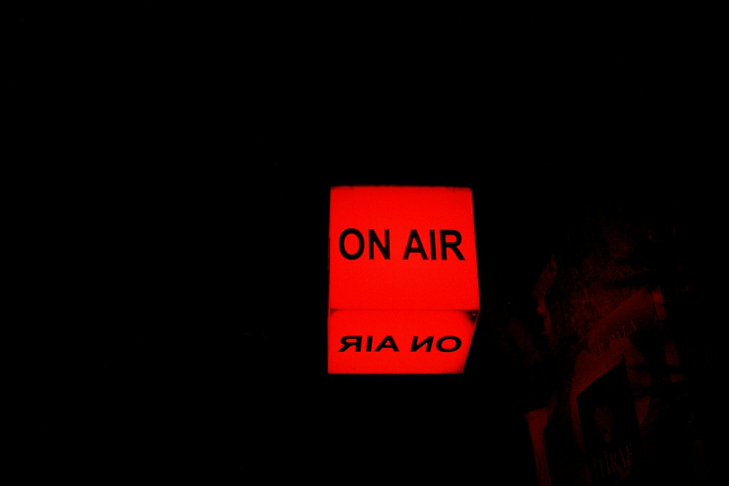 Glowing red on air sign reflecting on a dark surface.