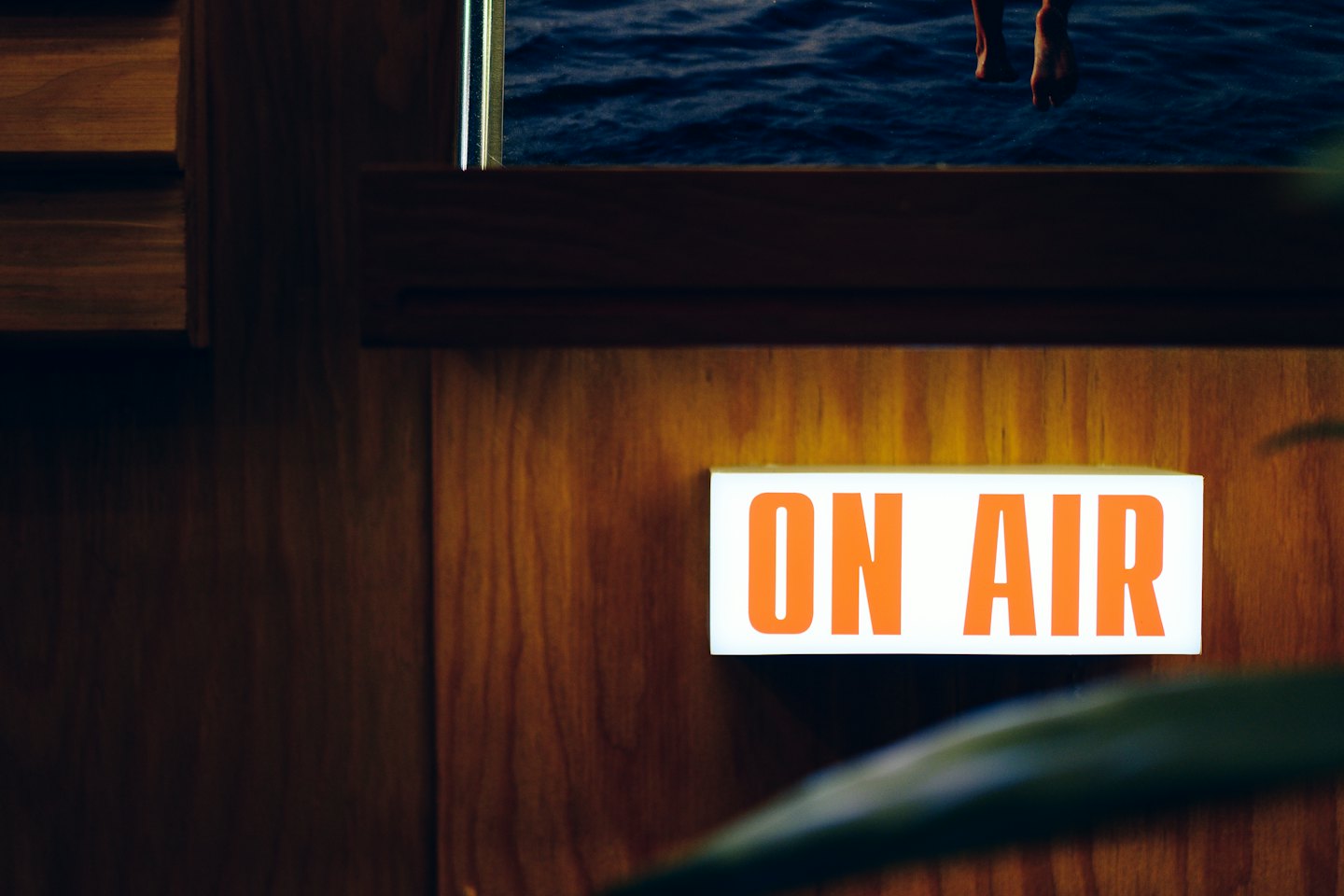 Orange ON AIR sign glows on a wooden wall above bare feet.